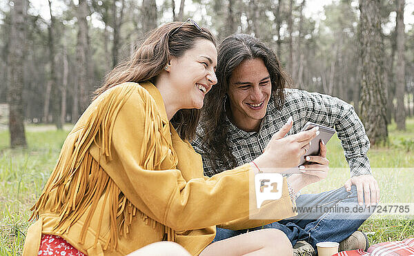 Fröhlicher Mann und Frau schauen auf ein digitales Tablet während einer Party im Wald