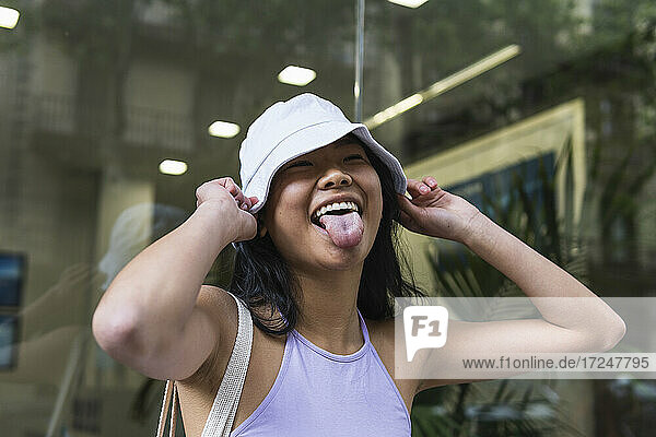 Woman sticking out tongue while holding bucket hat outdoors