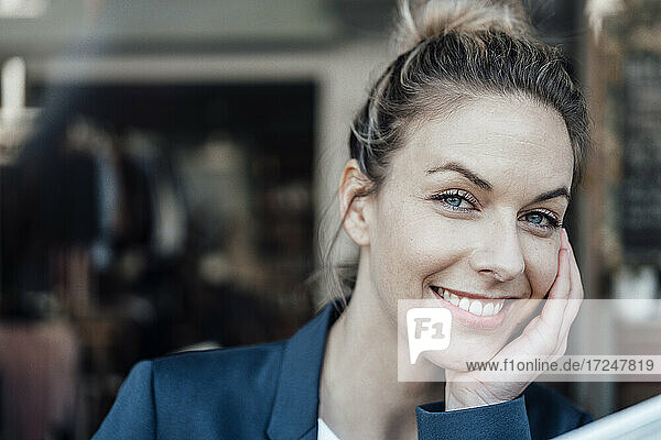 Lächelnde mittelalte Geschäftsfrau mit Hand am Kinn in einem Café