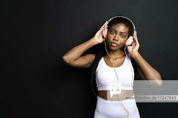 Junge Frau in Sportkleidung  die Kopfhörer trägt und vor einem schwarzen Hintergrund steht