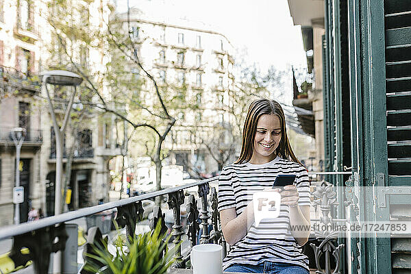 Glückliche Frau  die ihr Smartphone benutzt  während sie auf dem Balkon sitzt