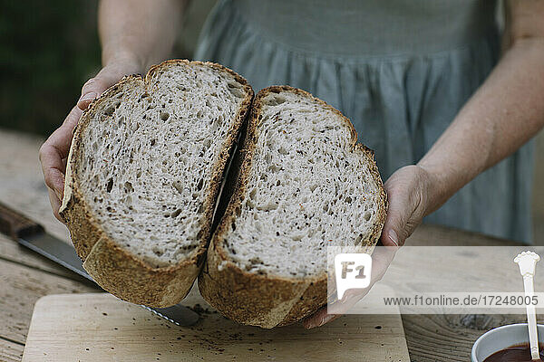Reife Frau zeigt halbiertes Brot auf dem Tisch