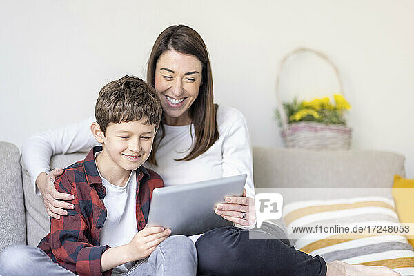 Lächelnder Junge und Mutter verwenden digitales Tablet auf dem Sofa zu Hause