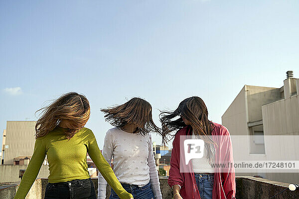 Freundinnen  die sich auf einer Gebäudeterrasse stehend die Haare in den Wind blasen