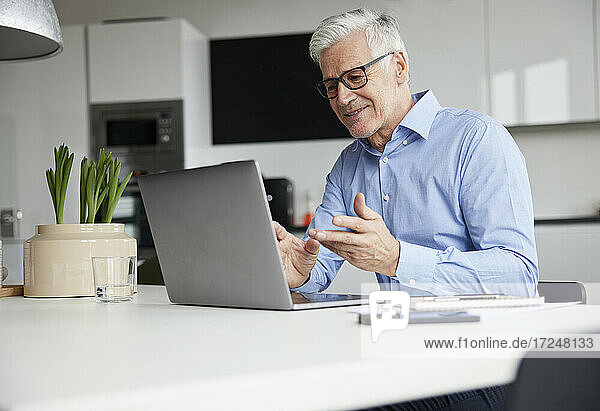 Lächelnder Unternehmer  der über einen Laptop im Büro ein Videogespräch führt