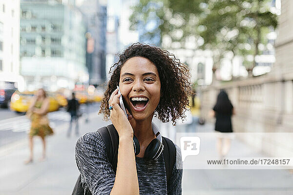 Frau lacht  während sie in der Stadt mit einem Smartphone telefoniert
