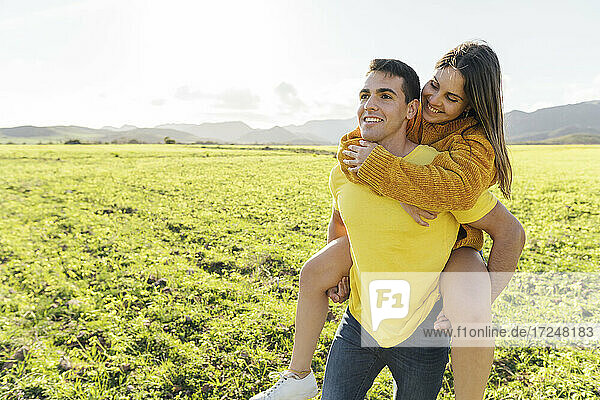 Boyfriend piggybacking girlfriend on meadow during sunny day