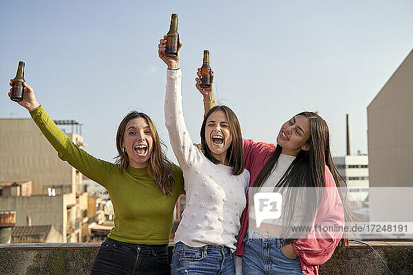 Glückliche Freundinnen heben Bierflaschen und genießen auf dem Dach