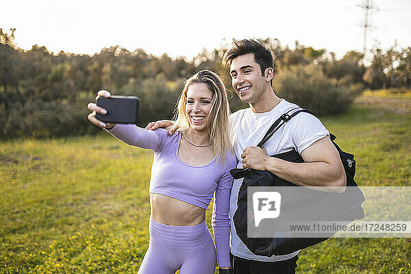 Smiling athletes taking selfie through mobile phone during sunset