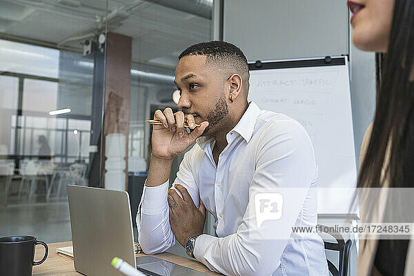 Nachdenklicher Geschäftsmann  der wegschaut  während er neben einer Kollegin in einem Coworking-Büro sitzt
