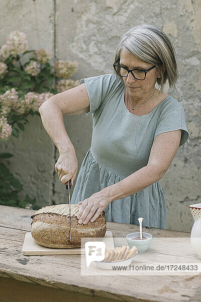 Ältere Frau schneidet Brot auf einem Tisch im Hinterhof