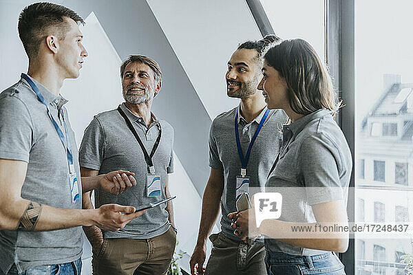 Lächelnde männliche und weibliche Fachkräfte  die während einer Konferenz auf einen Kollegen mit einem digitalen Tablet schauen