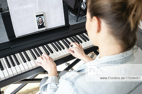 Mid adult woman on video call while practicing piano at home
