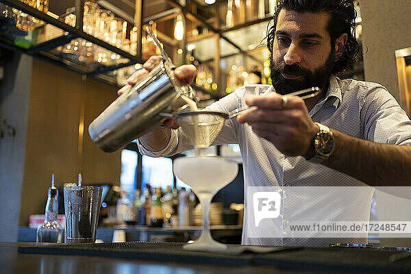Junger männlicher Barkeeper gießt am Bartresen ein Getränk in ein Glas