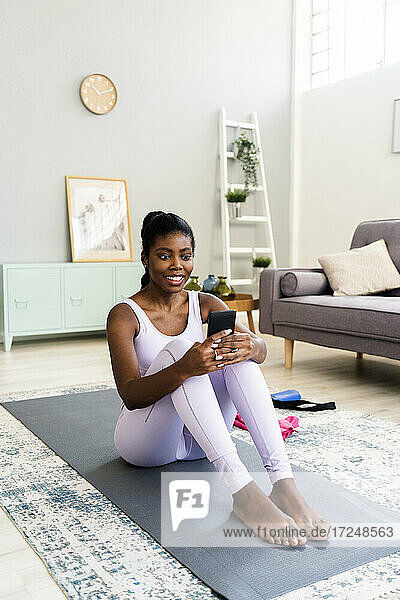 Smiling woman using smart phone on exercise mat at home