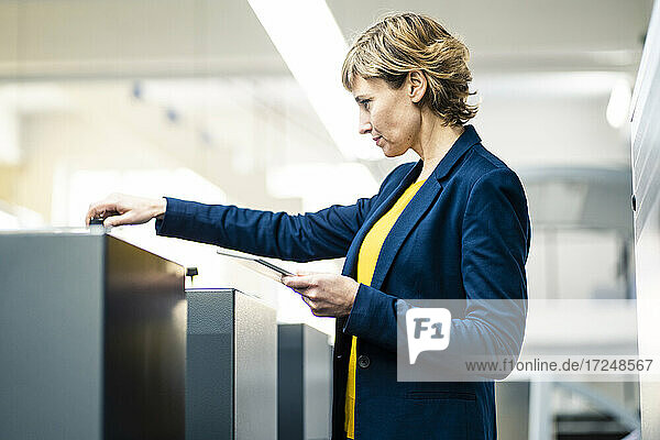 Weibliche Fachkraft mit digitalem Tablet  die eine Maschine in einer Druckerei bedient