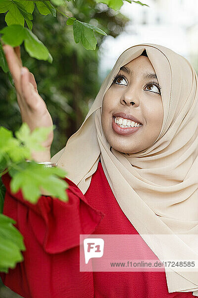 Lächelnde Frau mit Hidschab  die ein Blatt berührt