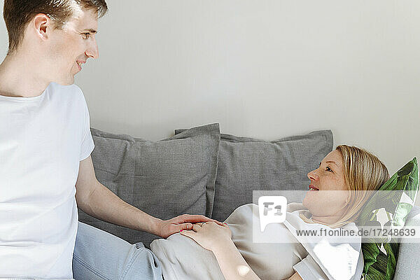 Fürsorglicher Ehemann betrachtet seine schwangere Frau auf dem Sofa im Wohnzimmer liegend