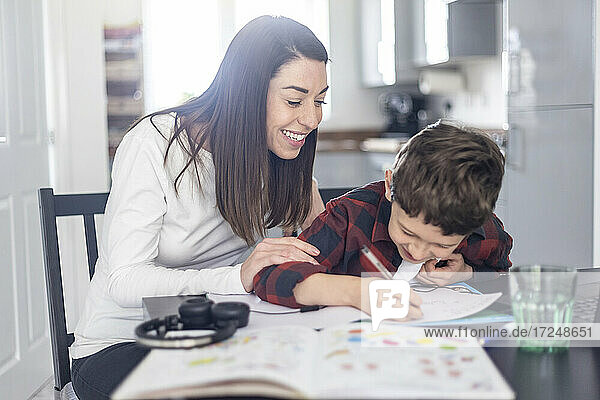 Lächelnde Mutter hilft ihrem Sohn bei den Hausaufgaben zu Hause