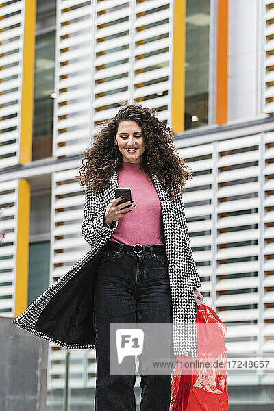 Lächelnde Frau mit Tasche und Mobiltelefon