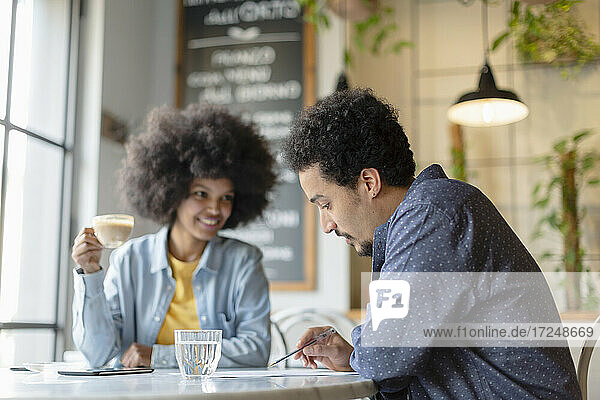 Männlicher Kunde liest Vertrag  während er mit einer Unternehmerin in einem Café sitzt