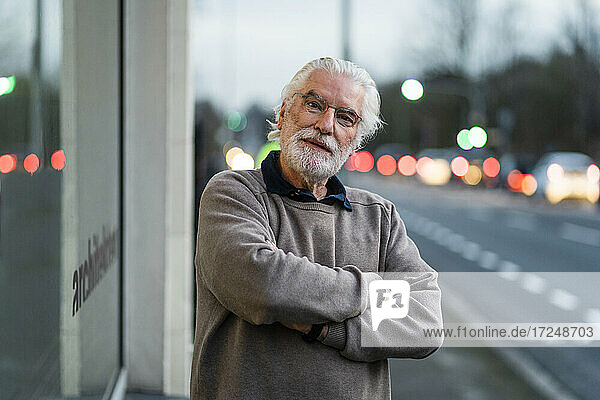 Älterer Mann mit verschränkten Armen vor einem Cafe stehend