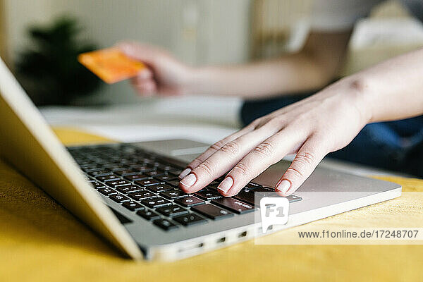 Woman doing online shopping through laptop while holding credit card at home