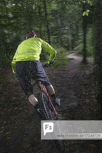 Mann fährt Fahrrad auf unbefestigtem Weg im Wald bei Regen