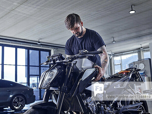 Young male expertise installing motorcycle part at workshop