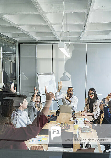 Multiethnische Gruppe von männlichen und weiblichen Fachkräften mit erhobenen Händen während einer Sitzung im Büro