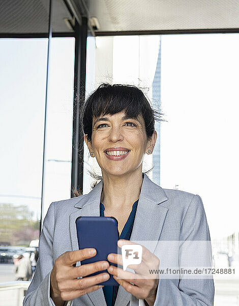 Weibliche Fachkraft lächelt  während sie ein Mobiltelefon am Eingang hält