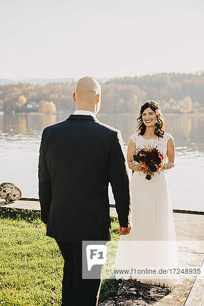 Glückliche Braut schaut Bräutigam an  während sie am See steht