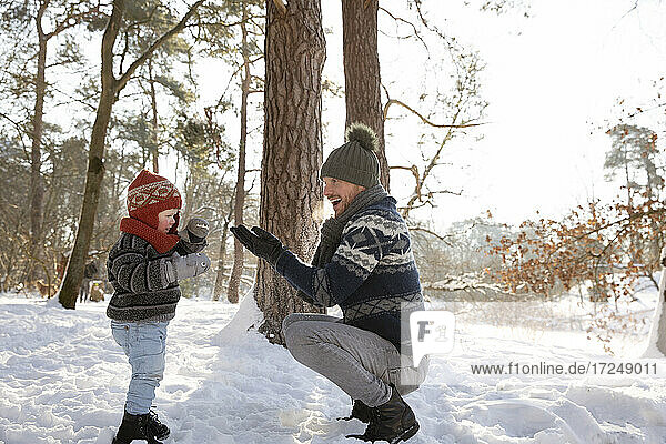 Father playing with son while crouching on snow during winter