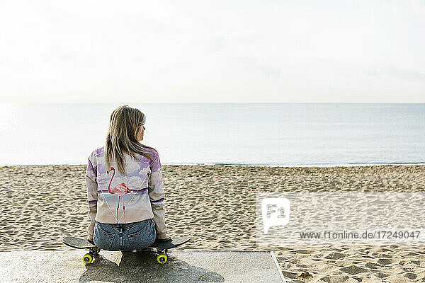 Mittlere erwachsene Frau sitzt auf einem Skateboard am Strand