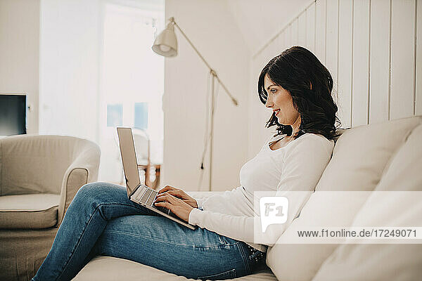 Freelancer woman using laptop while sitting on sofa at home