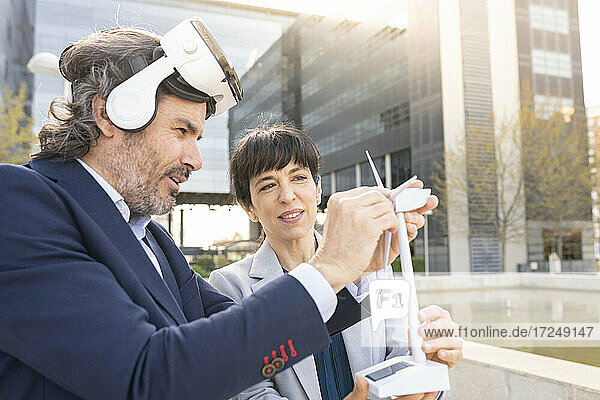 Männlicher Ingenieur mit Virtual-Reality-Headset,  der das Modell einer Windkraftanlage einstellt,  während eine Kollegin daneben steht