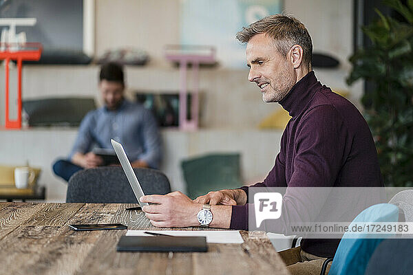 Männlicher Berufstätiger arbeitet am Laptop über dem Tisch am Arbeitsplatz