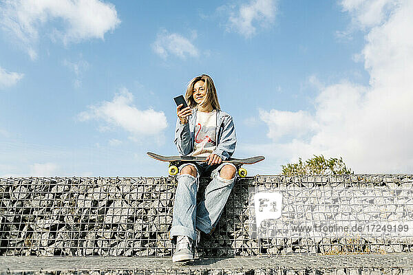 Lächelnde Frau mit Mobiltelefon an einer Felswand sitzend
