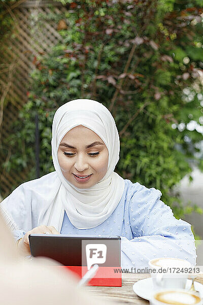 Smiling woman wearing hijab using digital tablet at sidewalk