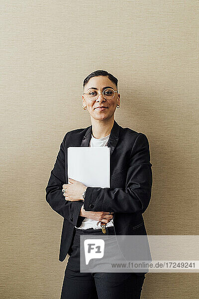 Lächelnder Fachmann  der ein Dokument hält  während er vor einer Wand steht
