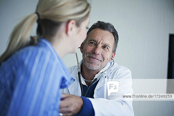 Lächelnder männlicher Oberarzt  der eine Patientin mit Stethoskop im Krankenhaus untersucht