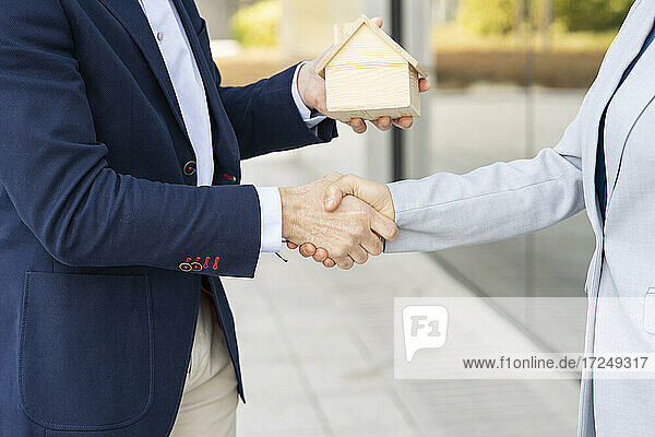 Geschäftsfrau beim Händedruck mit Immobilienmakler  der ein Architekturmodell hält