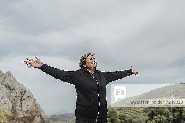Sorglose ältere Frau mit ausgestreckten Armen auf einem Berg stehend