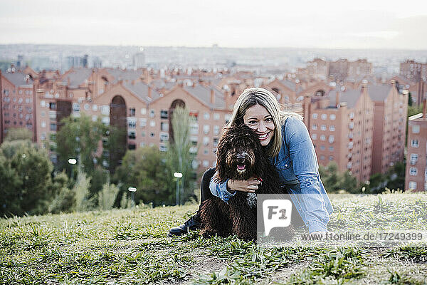 Glückliche Frau  die einen spanischen Wasserhund vor einer Stadtlandschaft umarmt