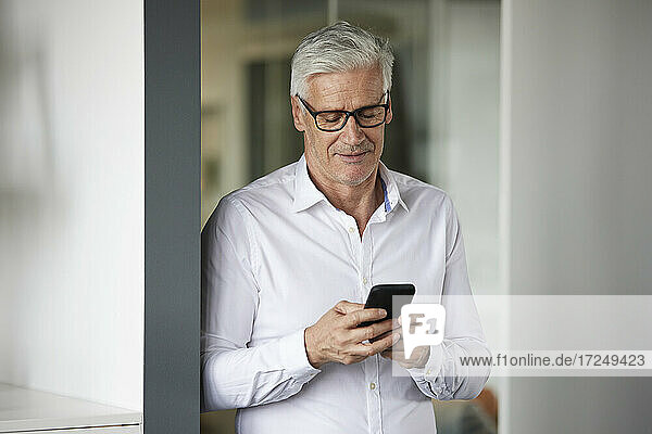Geschäftsmann  der ein Mobiltelefon benutzt  während er im Büro steht