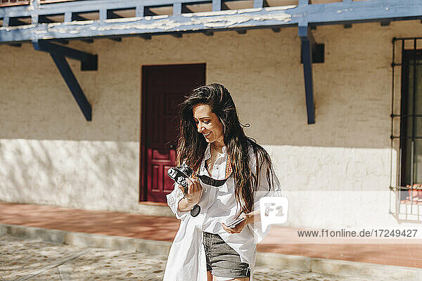 Frau lächelt  während sie die Kamera in einem Dorf an einem sonnigen Tag hält