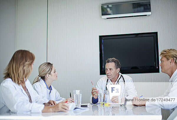 Oberarzt im Gespräch mit männlichen und weiblichen Mitarbeitern des Gesundheitswesens während einer Besprechung im Krankenhaus