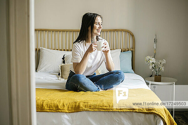 Lächelnde Frau mit Kaffee auf dem Bett zu Hause