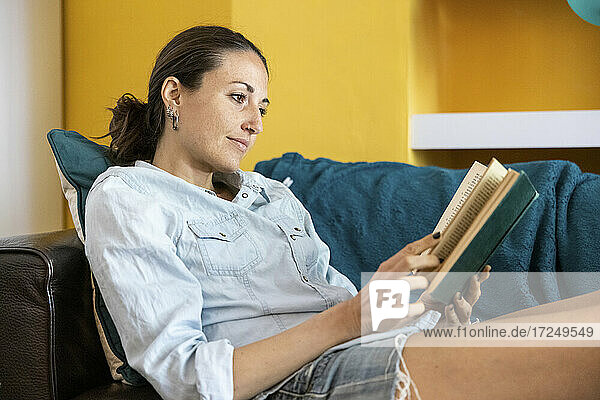 Frau liest ein Buch  während sie zu Hause auf dem Sofa sitzt