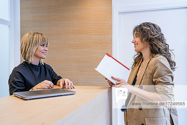 Smiling female receptionist looking at patient holding report in clinic